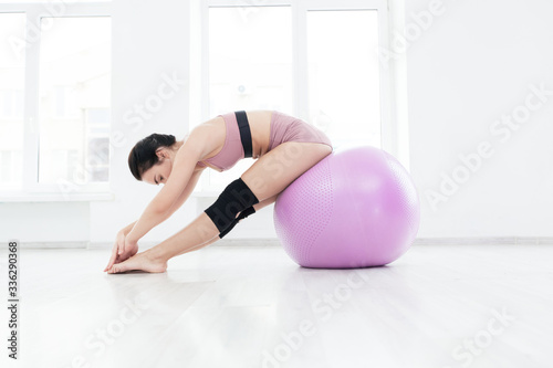 Slim sporty girl does stretching exercise reaching for her toes sitting on fitness ball
