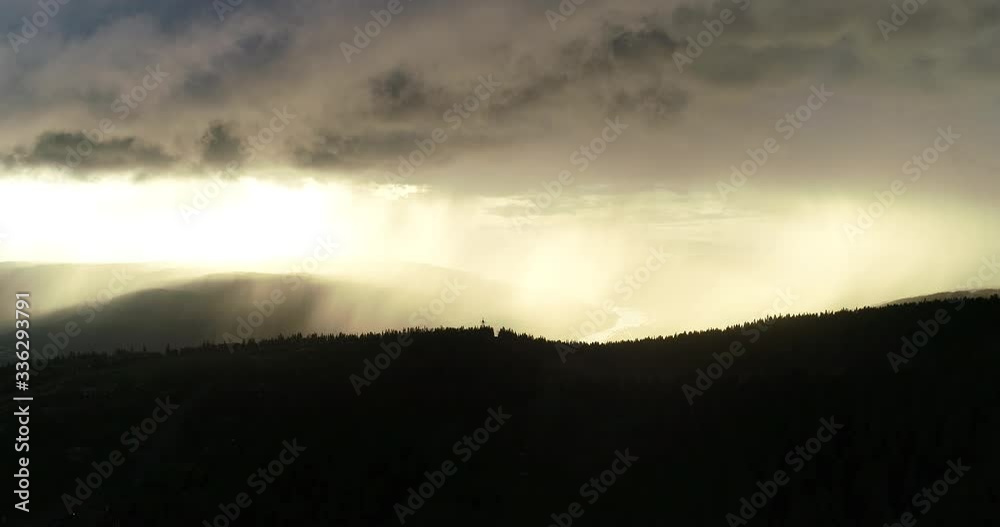 Aerial view of epic dramatic storm and rain over idyllic beautiful valley and mountains during sunset.