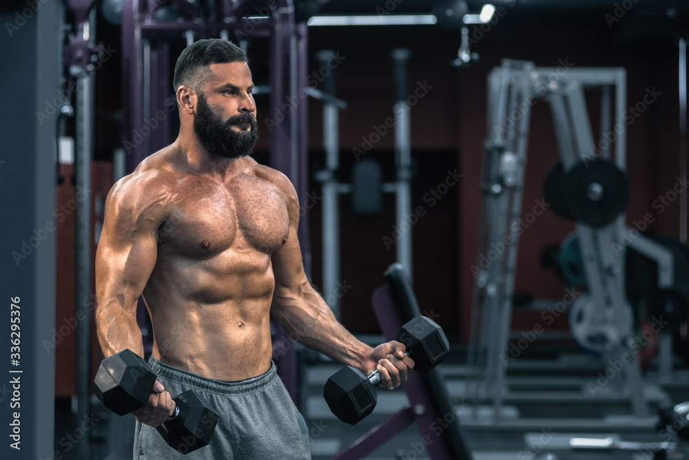 Muscular athletic bodybuilder working hard in gym on dark background