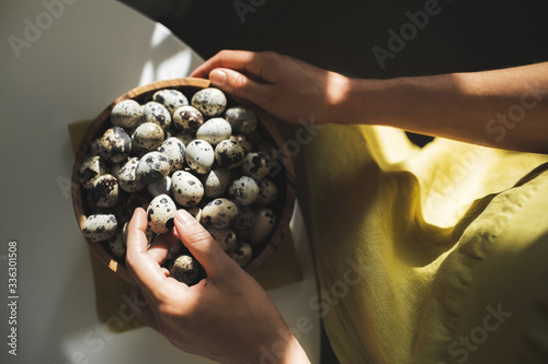 Woman hands holding wooden bowl with quail eggs. Dark background, beautiful natural sun light in kitchen. Easter cooking concept.