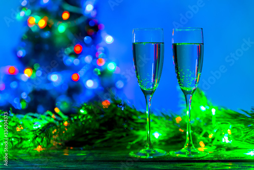 Glasses of champagne in a festive atmosphere, close-up. Christmas lights and two glasses on the background of a fir tree