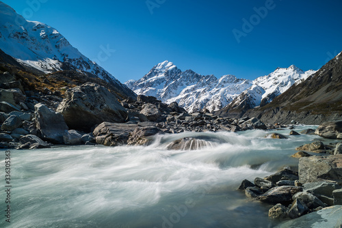 Glacier water flowing down a river surrounded by jagged rock formations and snow covered mountains in the background at Hooker Valley glacier at Mount Cook in New Zealand