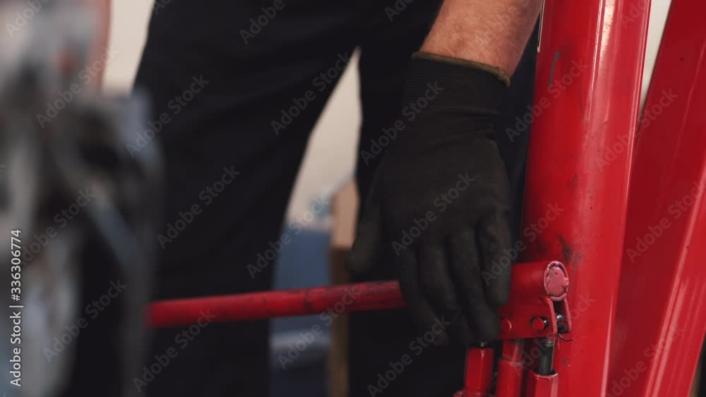 Person wears black gloves. Man wears dark uniform. Worker moves red construction. Person wears black gloves. Man wears dark uniform. Worker moves red construction.