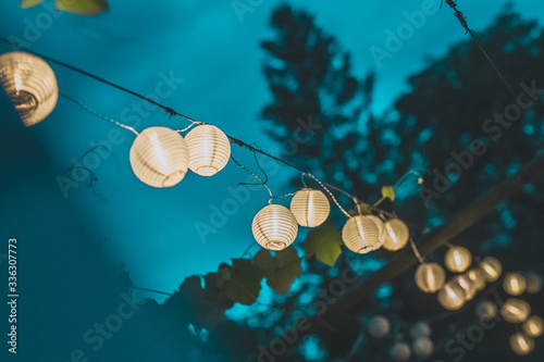 Canvas Print Row of round paper lanterns in a home garden on a wooden thatched background at night