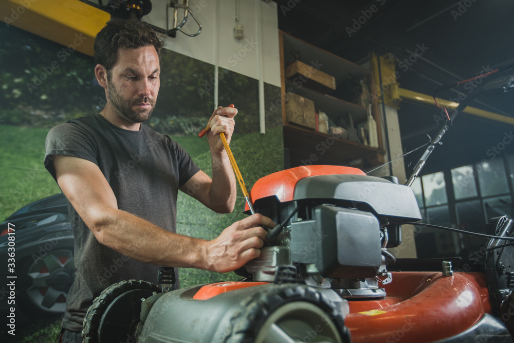 Professional serviceman is repairing a lawnmower, unscrewing a spark plug. Man repairing a mower in a workshop