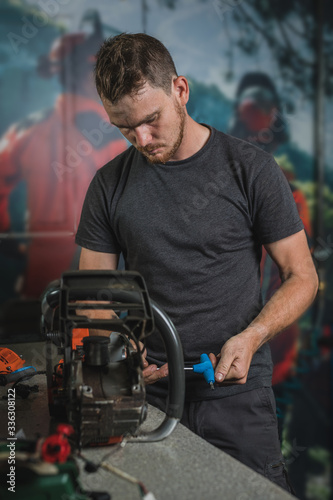 Professional serviceman is repairing a chainsaw using a spanner to untighten screw. Man fixing a chainsaw in a fancy workshop