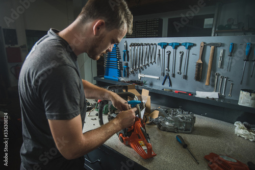 Professional serviceman is repairing a chainsaw using a spanner to untighten screw. Man fixing a chainsaw in a fancy workshop photo