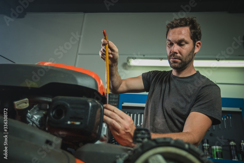 Professional serviceman is repairing a lawnmower, unscrewing a spark plug. Man repairing a mower in a workshop