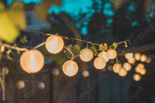 Row of round paper lanterns in a home garden on a wooden thatched background at night. Festive decoration in the garden on an evening.