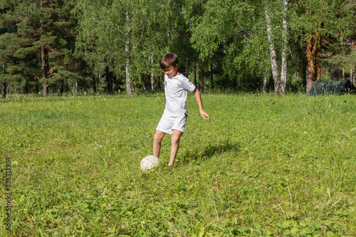 Boy in uniform plays football on meadow. Child run and kick soccer ball. Summer outdoor games