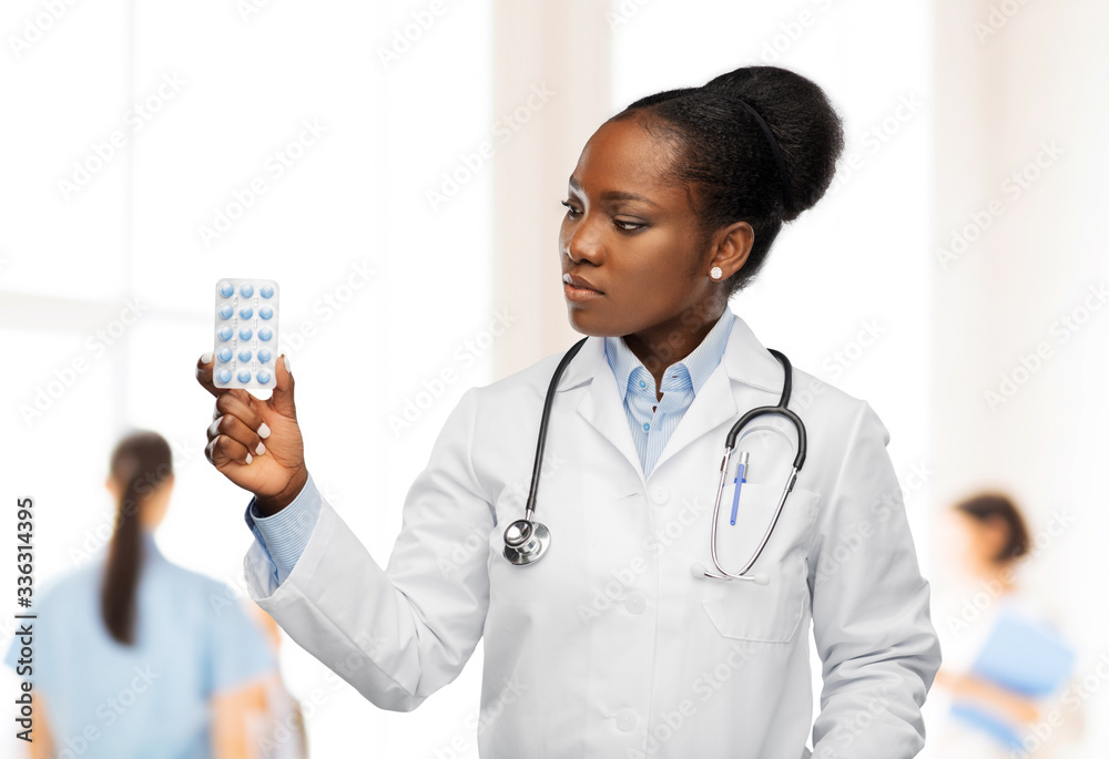 medicine, profession and healthcare concept - african american female doctor or in white coat with pills and stethoscope over hospital staff on background medicine, profession and healthcare concept - african american female doctor or in white coat with pills and stethoscope over hospital staff on background