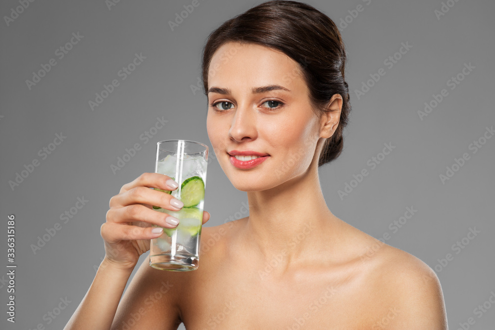 beauty and detox concept - woman drinking fresh water with cucumber and ice over grey background beauty and detox concept - woman drinking fresh water with cucumber and ice over grey background