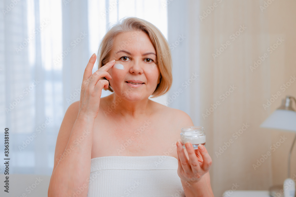 Smiling senior woman applying anti-aging lotion to remove dark circles under eyes. Smiling senior woman applying anti-aging lotion to remove dark circles under eyes.