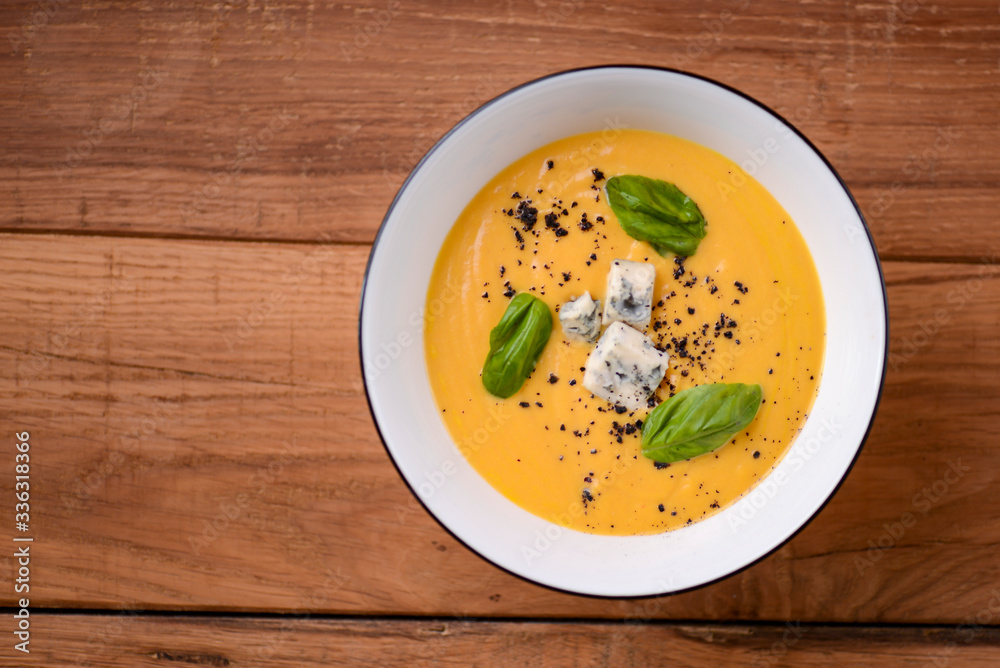 Creamy pumpkin soup topped cheese in a white bowl on a wooden table. Restaurant photography concept. Copy space. Creamy pumpkin soup topped cheese in a white bowl on a wooden table. Restaurant photography concept. Copy space.