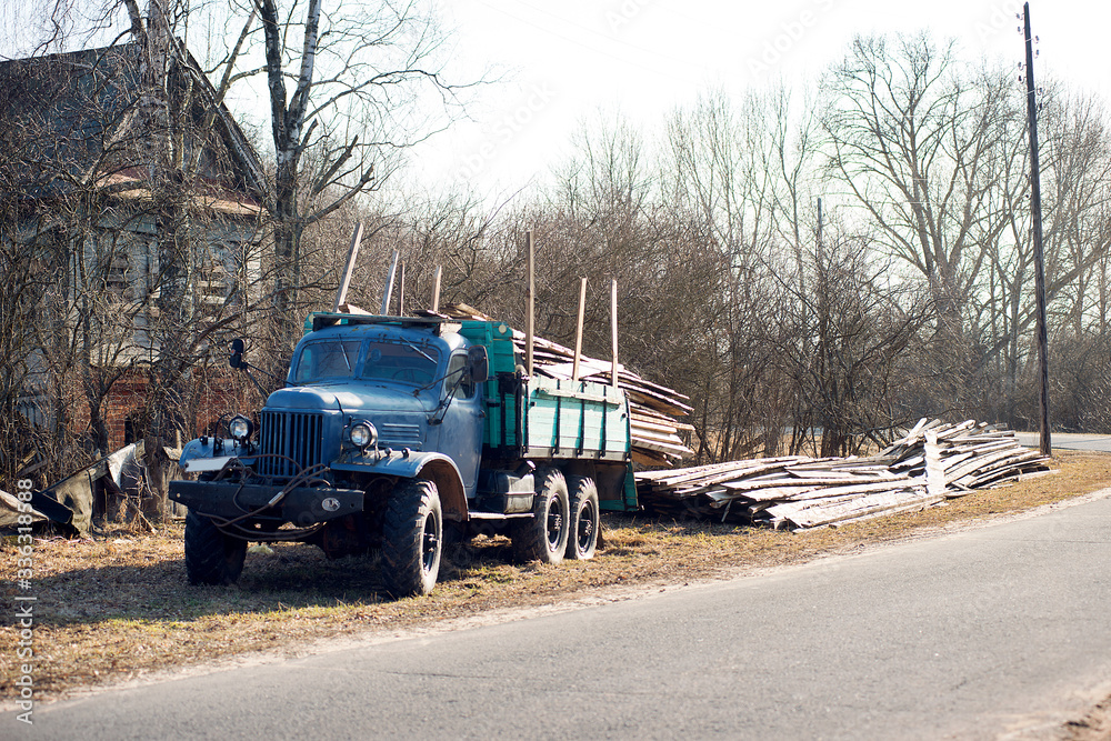 An old truck stands by the road in a village on a sunny day.