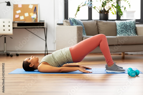 sport, fitness and healthy lifestyle concept - african american woman doing pelvic lift abdominal exercise at home photo