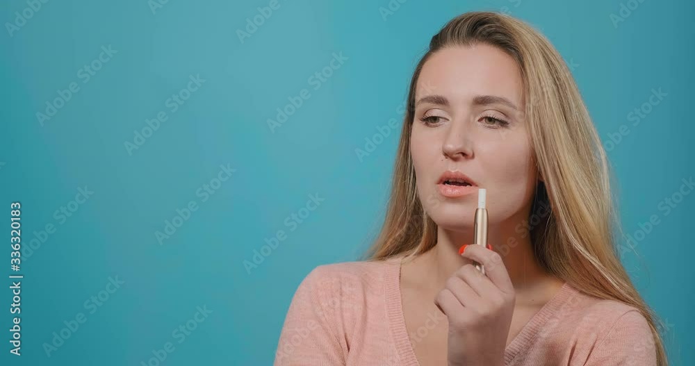 attractive blonde model with long loose hair smokes electronic cigarette and looks straight talking by blue wall close view attractive blonde model with long loose hair smokes electronic cigarette and looks straight talking by blue wall close view