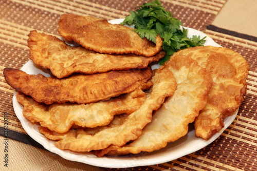 Chebureki or fried pie with beef meat on plate decorated with green parsley on bamboo mat background