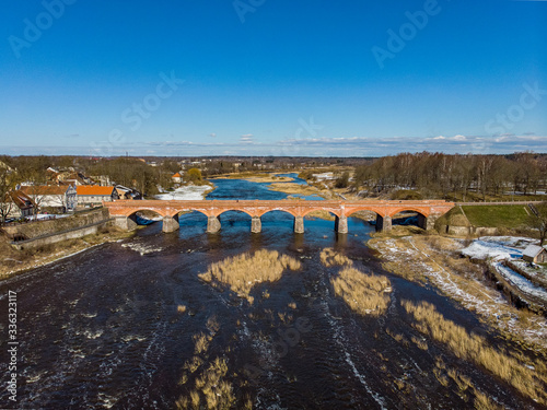 Beautiful sunny view of river wenta flowing towards old brick bridge in old historic countryside city Kuldiga. photo