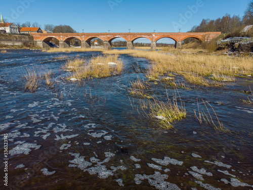 Beautiful sunny view of river wenta flowing towards old brick bridge in old historic countryside city Kuldiga. photo