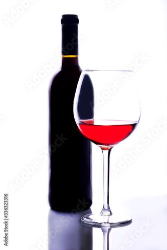  A thin-stemmed glass of red wine and a bottle of wine.