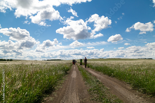 people walk in the distance on the road in the field, blue sky with clouds