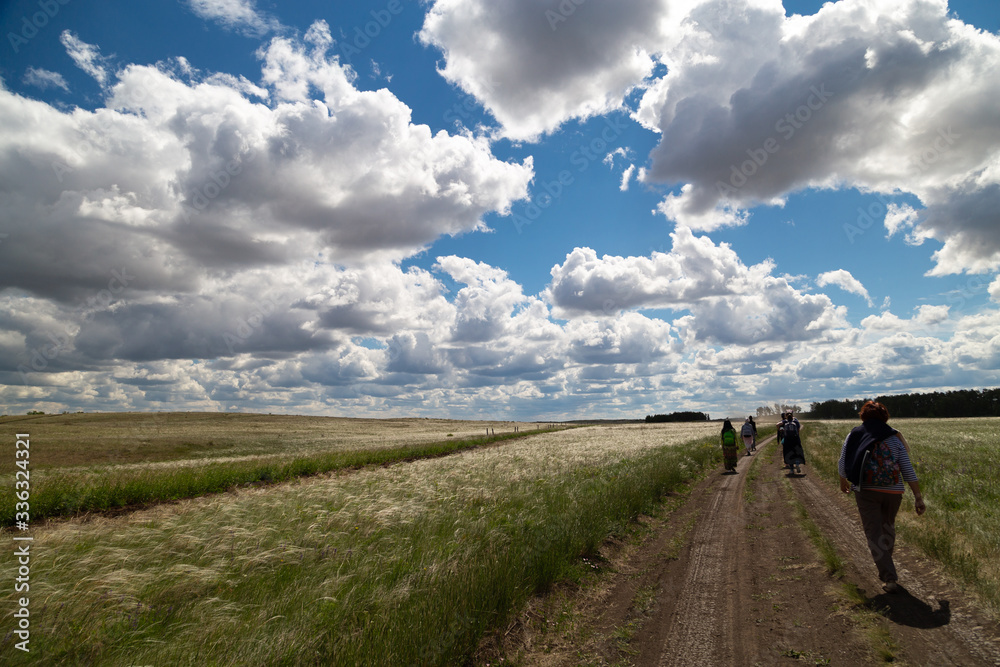 people walk in the distance on the road in the field, blue sky with clouds