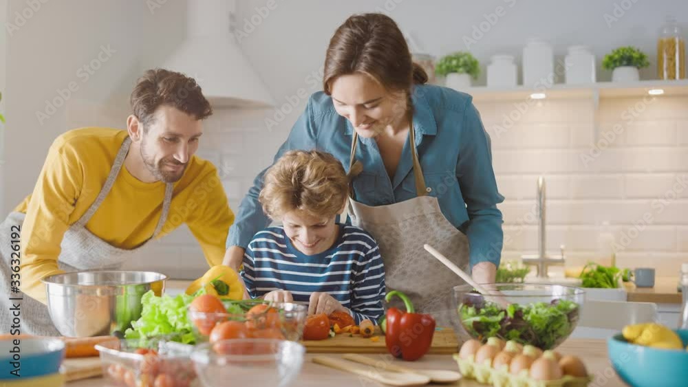 In Kitchen: Family of Three Cooking Together Healthy Dinner. Mother and Fathe Teach Little Boy Healthy Habits and to Cut Vegetables for Dinner Salad. Cute Child Helping their Beautiful Caring Parents In Kitchen: Family of Three Cooking Together Healthy Dinner. Mother and Fathe Teach Little Boy Healthy Habits and to Cut Vegetables for Dinner Salad. Cute Child Helping their Beautiful Caring Parents