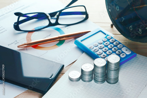 Top view coins stack and calculator and smartphne and gold pen and glasses decorate on working table. photo