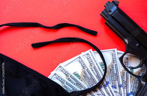 Gun, dollar money and protective medical mask on red background. Economy crisis, robbery, unemployment concept. Consequences of coronavirus people isolation during quarantine.