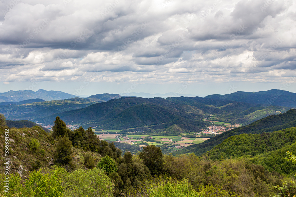 Heavy clouds hanging over the hill with flowers and mountains covered by the forest. Nature landscape. Ridges of the mountains at the background