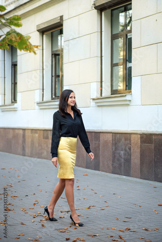 portrait of a young elegant business woman walking along a street building