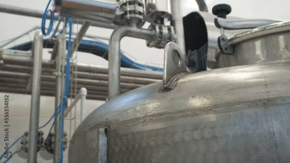 Pipes are intertwined and fastened together. All pipes lead into a large container with a lid. Above them is a metal platform for wires, eliminating their twisting. Details of one machine at factory. Pipes are intertwined and fastened together. All pipes lead into a large container with a lid. Above them is a metal platform for wires, eliminating their twisting. Details of one machine at factory.