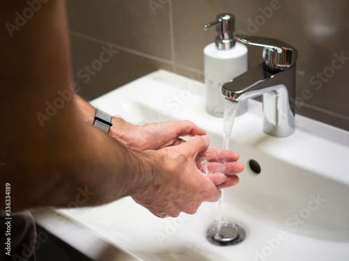 Men washing hands rubbing with soap in the bathroom sink.