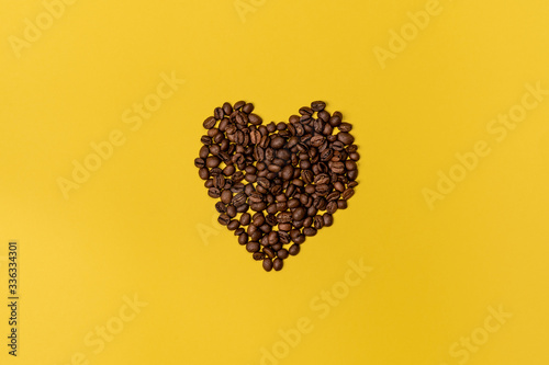 A handful of heart-shaped coffee beans in the center of the frame on a yellow background