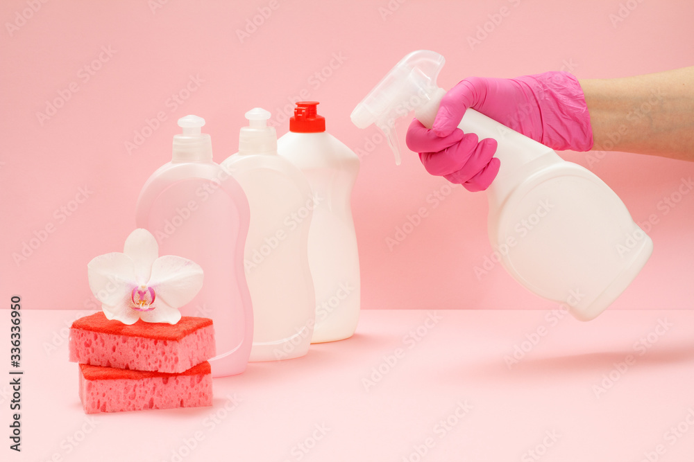 Bottles of washing liquid, sponges and hand with a bottle of glass cleaner on a pink background. Bottles of washing liquid, sponges and hand with a bottle of glass cleaner on a pink background.