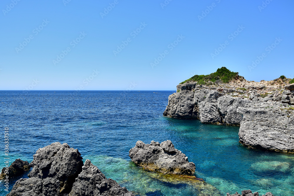Paleokastritsa / Corfu, Greece - Gray rocks in the blue-turquoise water of the Ionian Sea near Limni Beach, blue sky, in the summer during the daytime.