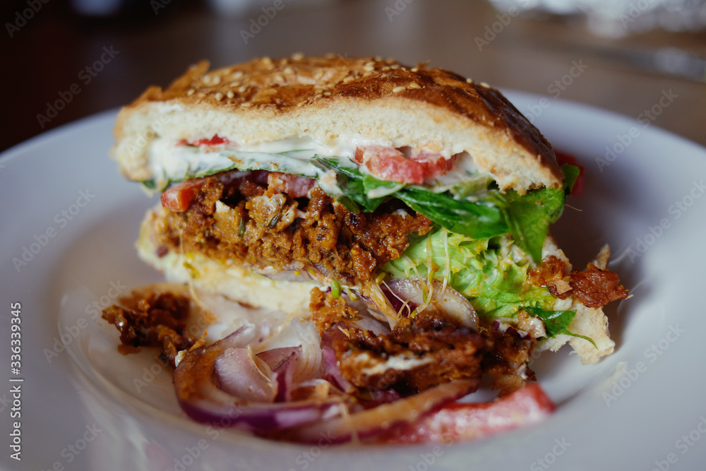 Vegetarian burger with seitan, tomato, lettuce, white bun with mayonnaise. Homemade veggie burger with seitan and sesame seeds, looks like a meat burger.