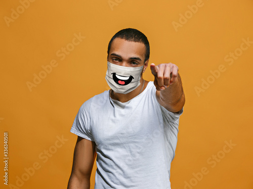 Pointing. Portrait of young african-american man with emotion on his protective face mask isolated on studio background. Beautiful male model. Human emotions, facial expression, sales, ad concept. photo