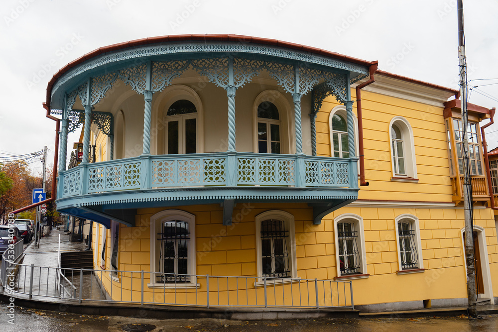 Sololaki area with old vintage houses. Blue wooden round ornamental balcony on a yellow small house. Raining, autumn.