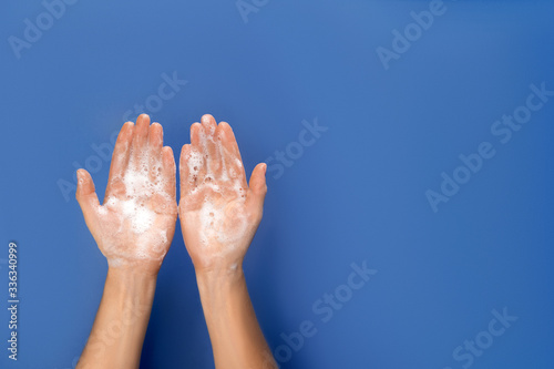 Wash your hand - coronavirus healthcare and hygiene concept. Flatlay photo of woman hands with soap foam on blue background.