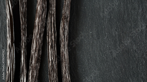Closeup detail on five vanilla beans on black slate board, view from above, empty space for text right side