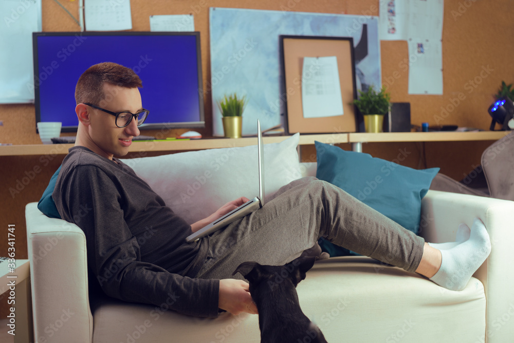 A man sits on a couch and works at a laptop. Homely atmosphere, the dog interferes, amuses the owner. A man works at home. Freelance, a man watches TV shows, on the screen, at home shopping. Dog. A man sits on a couch and works at a laptop. Homely atmosphere, the dog interferes, amuses the owner. A man works at home. Freelance, a man watches TV shows, on the screen, at home shopping. Dog.