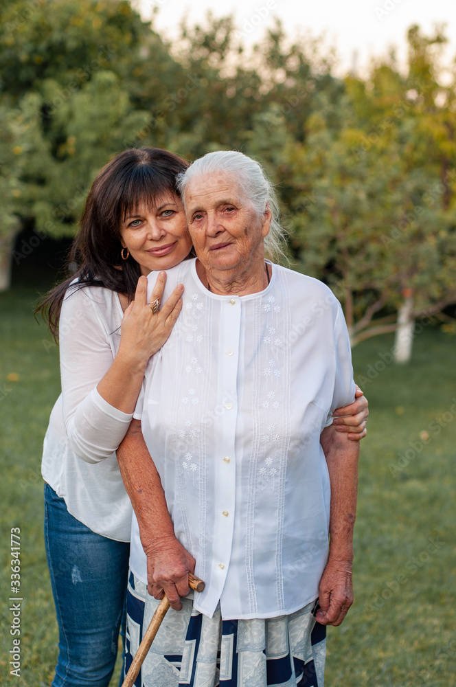 vertical closeup portrait of a ninety year old woman who is hugged from behind by her adult daughter