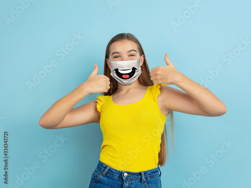 Thumb up. Portrait of young caucasian girl with emotion on her protective face mask isolated on studio background. Beautiful female model. Human emotions, facial expression, sales, ad concept.