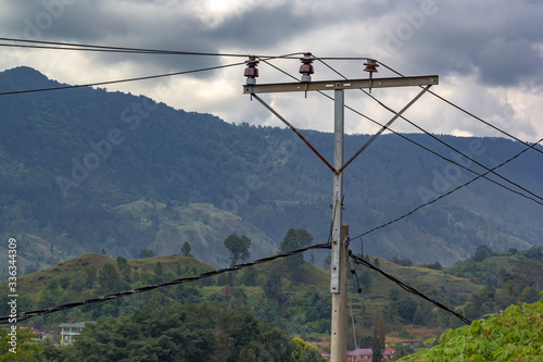 Home-made power pole with wires and old insulators against the backdrop of mountains and sky with clouds