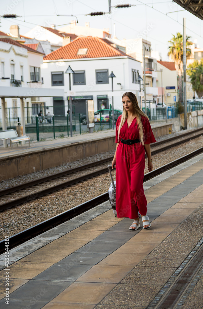 
Beautiful woman at the train station. A young woman dressed in a red suit with a suitcase walks to her train station. In a good mood with a smile on his face.