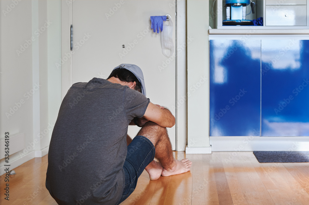 man sitting in front of the door of his house with a mask and safety gloves hanging on the doorknob. Coronavirus isolation concept man sitting in front of the door of his house with a mask and safety gloves hanging on the doorknob. Coronavirus isolation concept