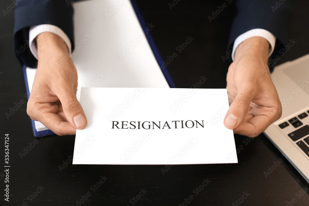 Office worker holding paper with text RESIGNATION at table Office worker holding paper with text RESIGNATION at table