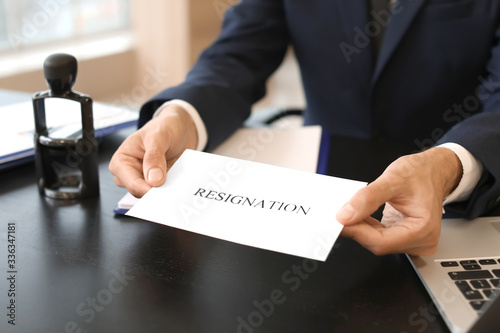 Office worker holding paper with text RESIGNATION at table